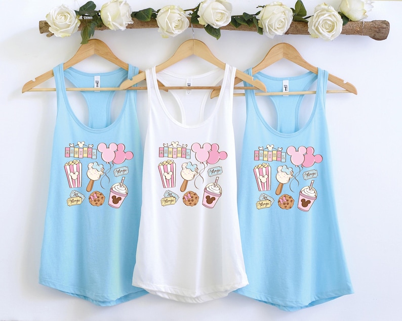 Pu&ograve; includere: Tre canottiere di colore azzurro chiaro, bianco e azzurro chiaro. Ogni canottiera presenta una stampa grafica di orecchie di Topolino, popcorn, un gelato di Topolino, un pretzel di Topolino e una tazza di Topolino. Il testo "Magic" &egrave; stampato su ogni canottiera.