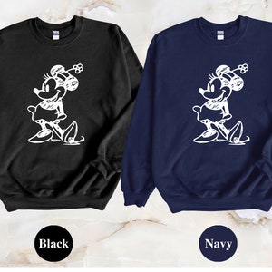 Puede incluir: Dos sudaderas con un gr&aacute;fico blanco de un rat&oacute;n de dibujos animados con un lazo. La sudadera de la izquierda es negra y la sudadera de la derecha es azul marino.