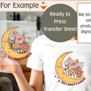 May include: A clear transfer sheet featuring a yellow crescent moon with a face, flowers, and the text "TAKE A MOMENT TO BREATHE." The design is also printed on a white t-shirt. The image also includes the text "Ready to Press Transfer Sheet."