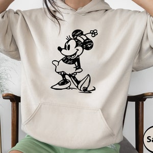 Puede incluir: Una sudadera con capucha de color arena con una ilustraci&oacute;n en blanco y negro de Mickey Mouse en la parte delantera. La ilustraci&oacute;n es un dibujo de estilo vintage de Mickey Mouse.