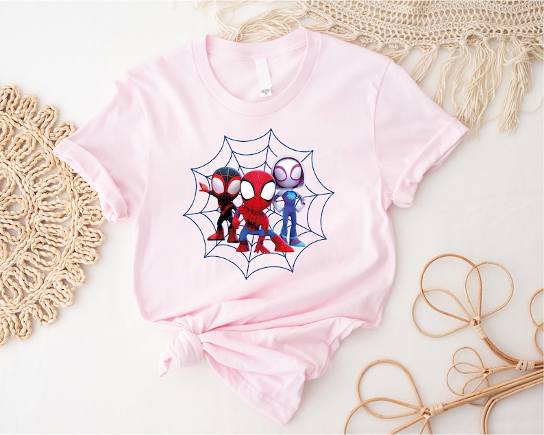 May include: Pink t-shirt with a graphic of three cartoon Spider-Man characters in a web. The characters are red, blue, and black.