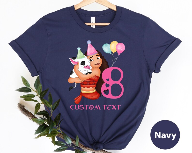 Pu&ograve; includere: Maglietta blu navy con un'illustrazione di cartone animato di una ragazza con un maiale, palloncini e il numero 8. Il testo "CUSTOM TEXT" &egrave; stampato sotto l'illustrazione.