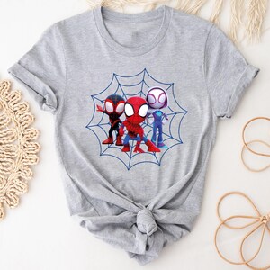 May include: Gray t-shirt with a graphic of three cartoon Spider-Man characters in a web. The characters are red, black, and white.