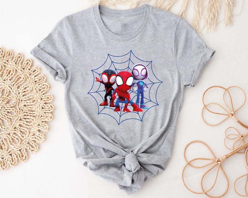 May include: Gray t-shirt with a graphic of three cartoon Spider-Man characters in a web. The characters are red, black, and white.