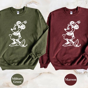 Puede incluir: Dos sudaderas con un contorno blanco de Minnie Mouse en la parte delantera. La sudadera de la izquierda es verde militar y la sudadera de la derecha es granate.