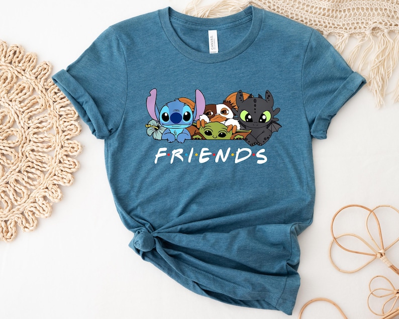 May include: Teal blue t-shirt featuring a graphic of cartoon characters Stitch, Baby Yoda, Toothless, and others. The word "FRIENDS" is printed in white below the characters. The shirt is made of a soft material and has rolled-up sleeves.