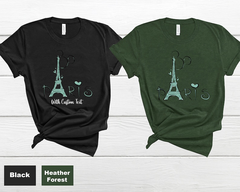 Op de afbeelding: Zwarte en heidegroene t-shirts met een turquoise Eiffeltoren-ontwerp en het woord "Paris". De tekst "With Custom Text" is ook inbegrepen. De shirts zijn gemaakt van een zacht materiaal.