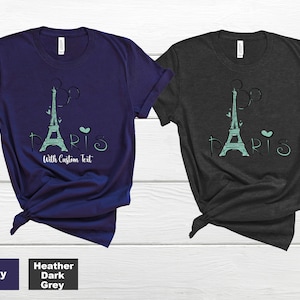 Op de afbeelding: Twee t-shirts, marineblauw en donkergrijs gem&ecirc;leerd, met een turquoise Eiffeltoren ontwerp, het woord "PARIS" en de tekst "With Custom Text". De shirts zijn gemaakt van zacht materiaal.