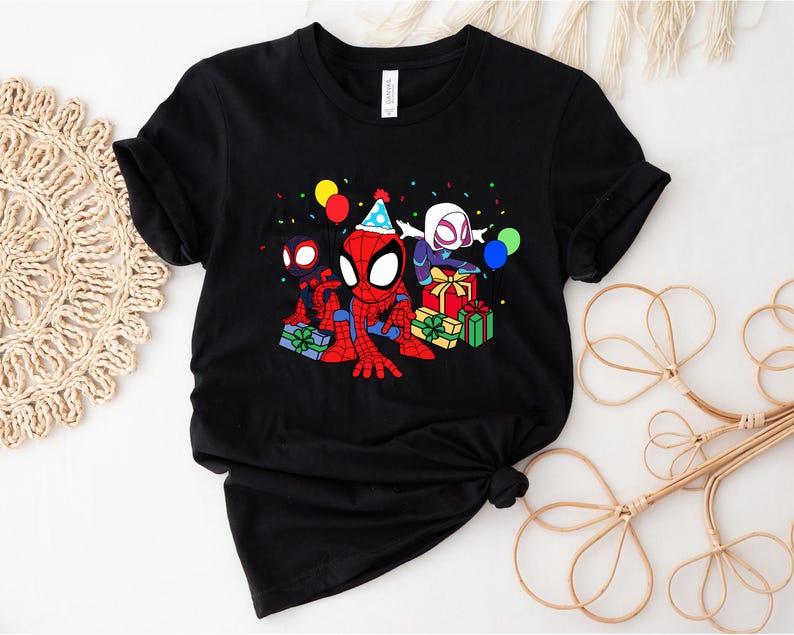 Puede incluir: Camiseta negra con una imagen de dibujos animados de Spider-Man, Spider-Gwen y otro personaje de Spider-Man celebrando un cumplea&ntilde;os con regalos y confeti.