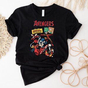 May include: Black t-shirt with a vibrant graphic of Disney characters in an Avengers theme. The design includes Mickey Mouse as Captain America, Iron Man, and other characters. The word "AVENGERS" is printed in red above the characters.