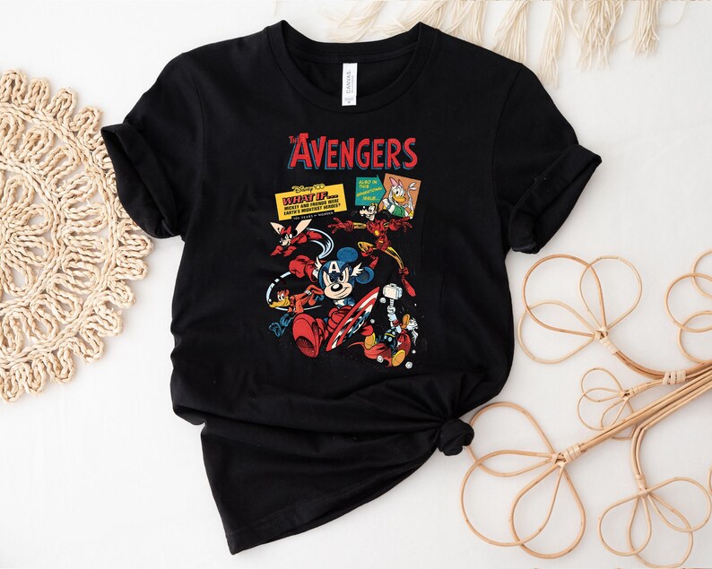 May include: Black t-shirt with a vibrant graphic of Disney characters in an Avengers theme. The design includes Mickey Mouse as Captain America, Iron Man, and other characters. The word "AVENGERS" is printed in red above the characters.