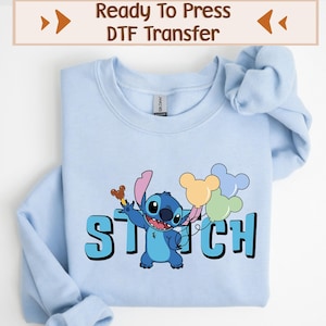 May include: Light blue sweatshirt featuring a graphic of the character Stitch holding balloons. The word "STITCH" is printed in large, blue letters below the character. The top of the image reads "Ready To Press DTF Transfer".