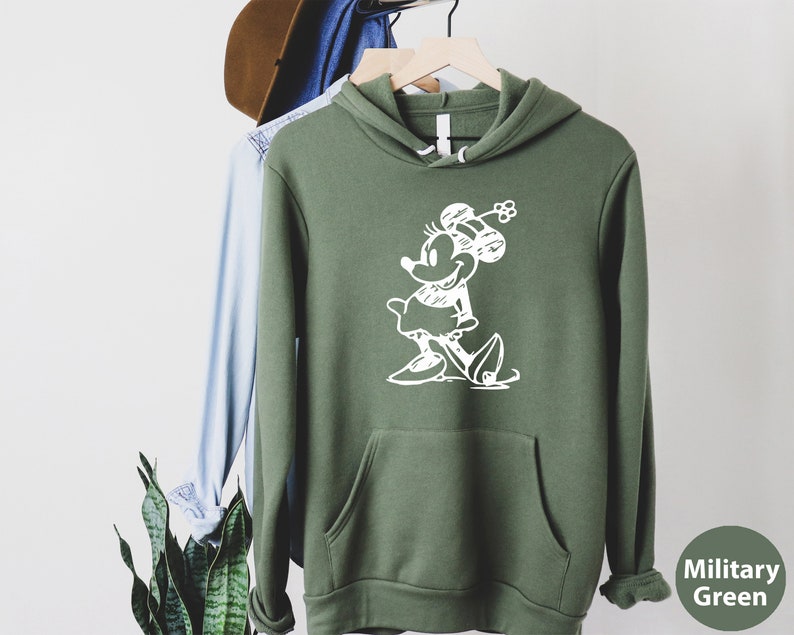 Puede incluir: Una sudadera con capucha verde con un contorno blanco de un rat&oacute;n de dibujos animados con un lazo. El texto "Military Green" est&aacute; en la esquina inferior derecha de la imagen.