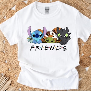 May include: White t-shirt featuring a graphic of cartoon characters including Stitch, Toothless, and others. The word "FRIENDS" is printed in black below the characters. The shirt is made of a soft material.