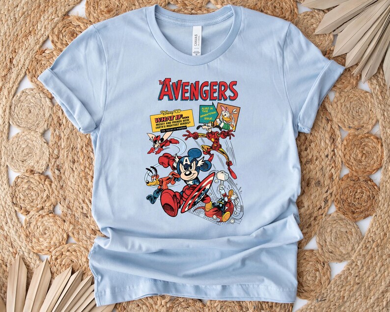 May include: Pale blue t-shirt with a vibrant graphic of Disney characters in an Avengers theme. The design includes Mickey Mouse, Donald Duck, and Iron Man, with the text "The Avengers" in red.