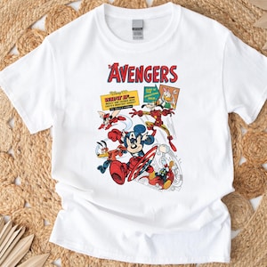 May include: White t-shirt with a vibrant graphic of Disney characters in an Avengers theme. The design includes Mickey Mouse with a shield, Donald Duck, and Iron Man. The word "AVENGERS" is in red.