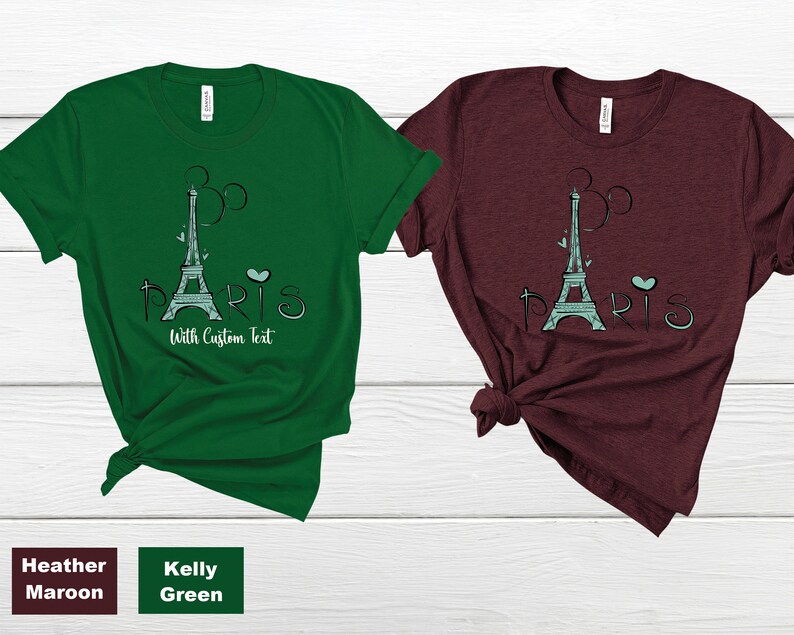 Op de afbeelding: Twee T-shirts, &eacute;&eacute;n in Kelly Green en &eacute;&eacute;n in Heather Maroon, elk met een afbeelding van de Eiffeltoren en het woord "PARIS". Het ontwerp bevat een hart en de tekst "With Custom Text".
