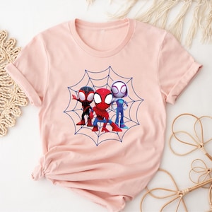 May include: A pink t-shirt with a graphic of three cartoon Spider-Man characters in a web. The characters are red, blue, and white.