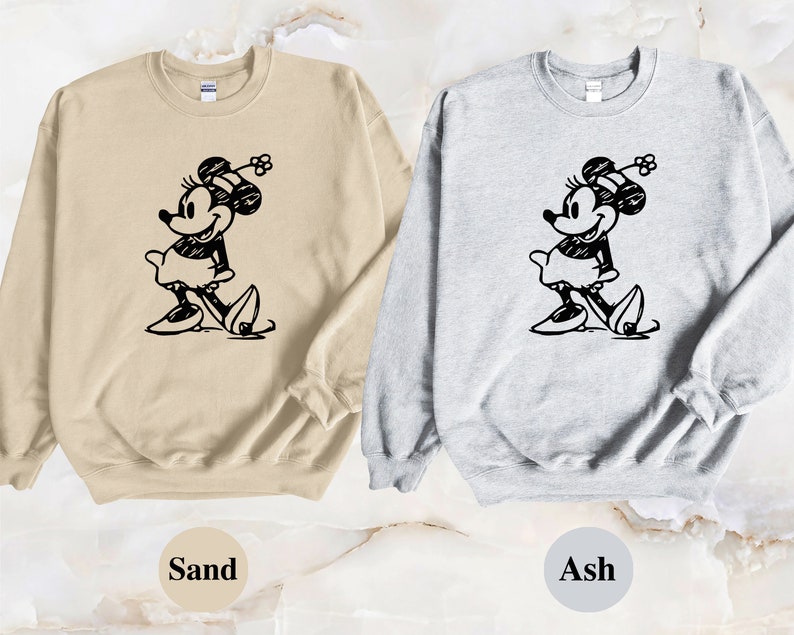 Puede incluir: Dos sudaderas con una ilustraci&oacute;n en blanco y negro de Mickey Mouse. La sudadera de la izquierda es de color arena y la sudadera de la derecha es de color ceniza.