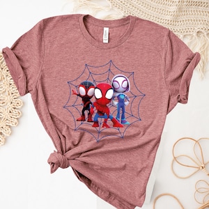 May include: A maroon t-shirt with a graphic of three cartoon Spider-Man characters in a web. The characters are red, black, and white.