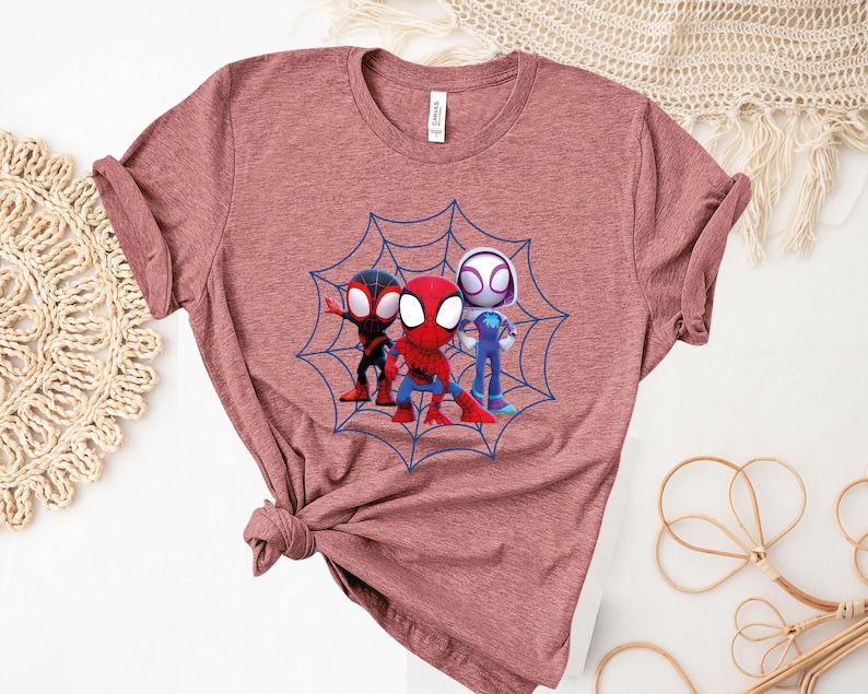 May include: A maroon t-shirt with a graphic of three cartoon Spider-Man characters in a web. The characters are red, black, and white.