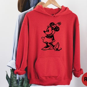 Puede incluir: Sudadera con capucha roja con una ilustraci&oacute;n en blanco y negro de Minnie Mouse con un sombrero y una falda.
