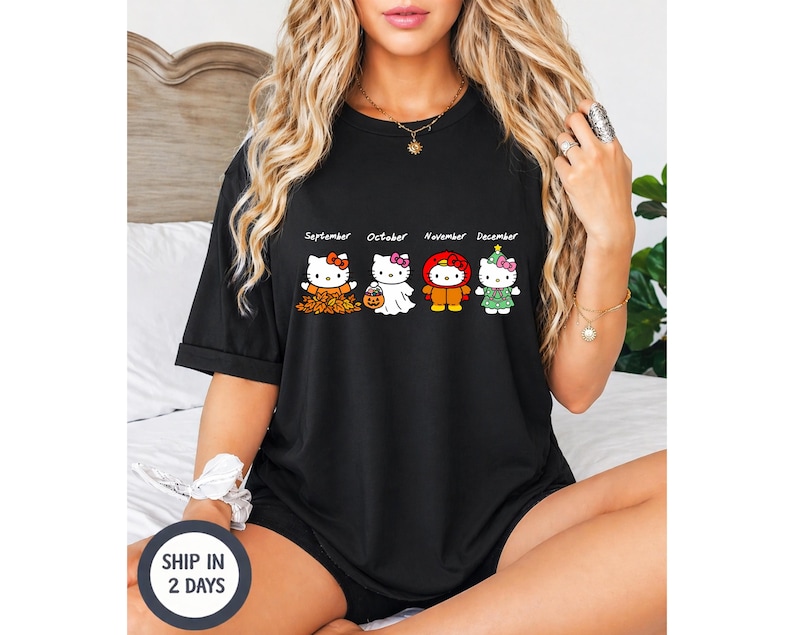 Puede incluir: Una camiseta negra de manga corta con un estampado gr&aacute;fico de cuatro personajes de Hello Kitty etiquetados como September, October, November y December. Los personajes visten trajes de temporada que representan hojas de oto&ntilde;o, un fantasma, un pavo y un &aacute;rbol.