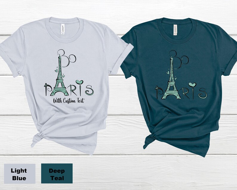 Op de afbeelding: Twee t-shirts, &eacute;&eacute;n lichtblauw en &eacute;&eacute;n diepblauwgroen, met een grafische afbeelding van de Eiffeltoren in zeegroen en het woord "Paris". Het ontwerp bevat hartjes en een op Mickey Mouse ge&iuml;nspireerd ontwerp. De tekst "With Custom Text" is ook inbegrepen.