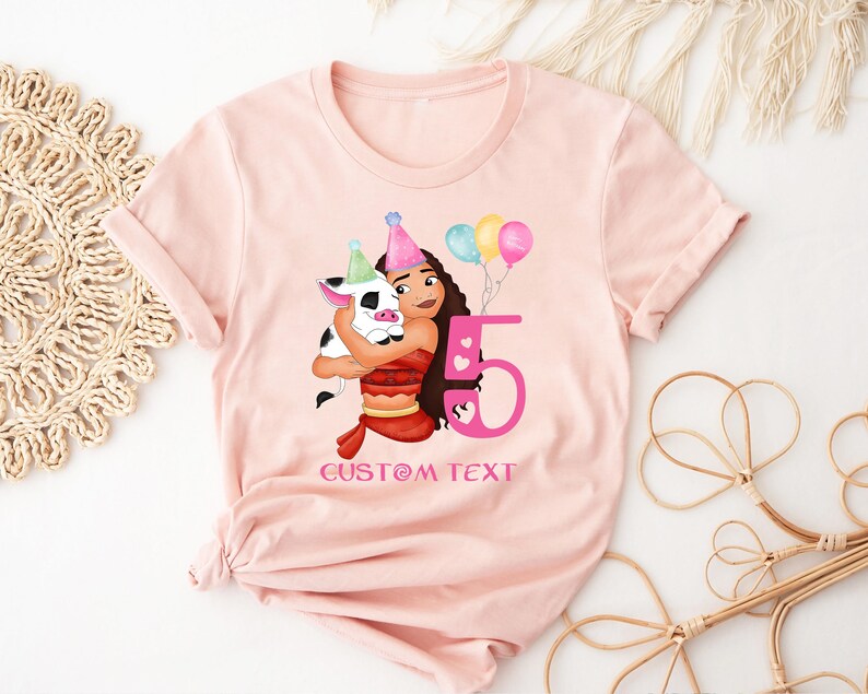 Pu&ograve; includere: Maglietta rosa con un'immagine di cartone animato di una ragazza con i capelli castani e un maiale. La ragazza indossa un vestito rosa e rosso e tiene un maiale. Il numero 5 &egrave; in rosa e il testo "CUSTOM TEXT" &egrave; sotto l'immagine.