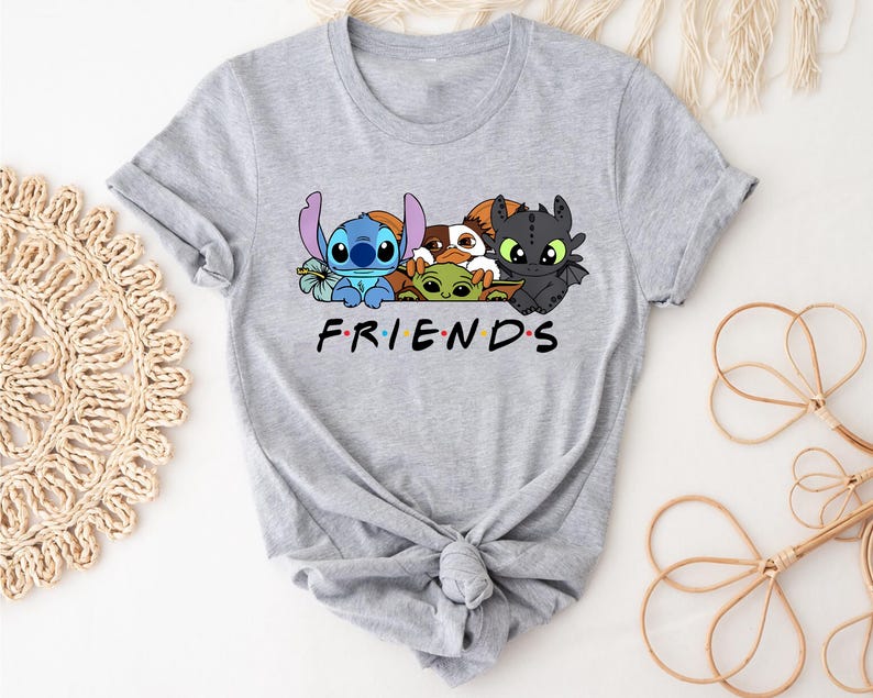 May include: A light gray t-shirt featuring a graphic of cartoon characters, including Stitch, Baby Yoda, and Toothless, above the word "FRIENDS" in a familiar font. The shirt is knotted at the bottom.