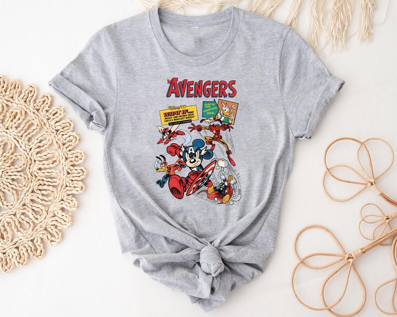 May include: A grey t-shirt with a vibrant graphic of Disney characters in an Avengers theme. The design showcases Mickey Mouse as Captain America, Donald Duck, and Iron Man, with the word "Avengers" in red at the top.