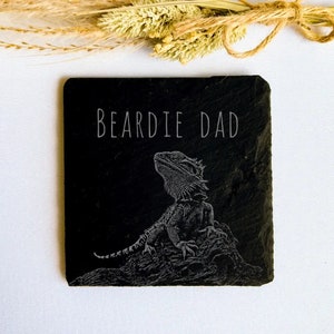 May include: Black slate coaster with a white engraved bearded dragon and the text "Beardie Dad".