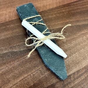 May include: A set of two black slate plant markers tied together with twine and a white chalk pencil.