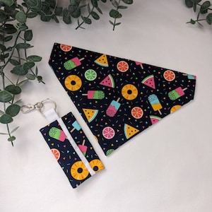 Può includere: Un set di accessori per animali domestici abbinato con bandana e portachiavi. Entrambi gli articoli sono decorati con illustrazioni colorate di frutta e ghiaccioli su sfondo blu scuro. Il portachiavi ha un cinturino bianco e hardware color argento.