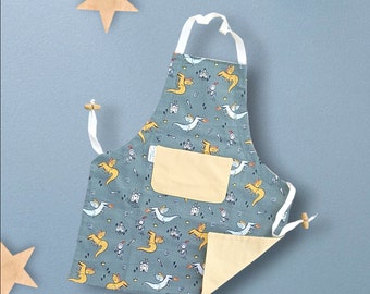 May include: A blue and yellow children's apron with a dragon and knight pattern. The apron has a large pocket on the front.