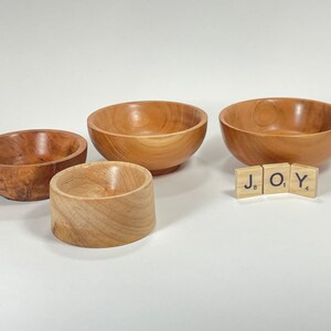 May include: Four wooden bowls of varying sizes, with the smallest bowl nested inside the second smallest bowl. The word "JOY" is spelled out using three wooden letter tiles.