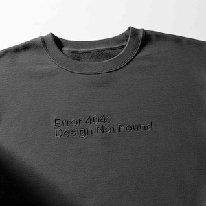 Puede incluir: Sudadera gris oscuro con el texto "Error 404: Design Not Found" en relieve en la parte delantera. La sudadera de cuello redondo está hecha de un material suave y es de estilo casual.