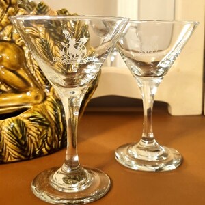 May include: Two clear glass martini glasses with etched logos. The glass on the left has the text "The Babycham Co."