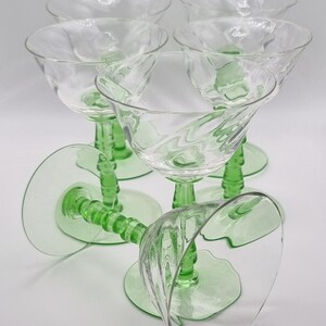 May include: Set of six green glass stemmed champagne coupes with a clear glass bowl. The glasses have a fluted design and a green stem with a ribbed pattern.