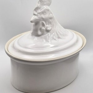 May include: White ceramic oval casserole dish with a rooster-shaped lid. The dish has a smooth, glossy finish.