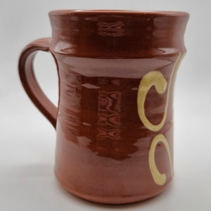 May include: A brown ceramic mug with a yellow swirl design. The mug has a handle and a rounded shape.