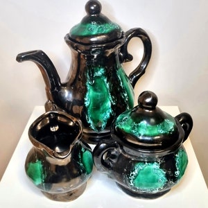 May include: A black and green ceramic tea set comprising a teapot, creamer, and sugar bowl. The set features a distinctive marbled glaze with green accents.