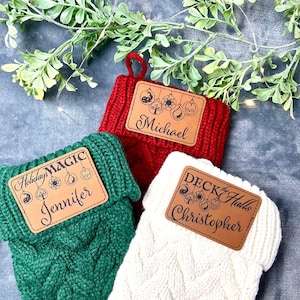 May include: Three knitted stockings with personalized tags. The tags are brown with black text and images. The stockings are red, green, and white. The tags read "Holiday Magic Jennifer", "Deck the Halls Christopher", and "Michael".