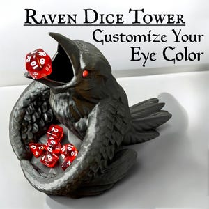 May include: A black raven dice tower with red eyes. The raven is holding dice in its wings and mouth. The text "Customize Your Eye Color" is written above the raven.
