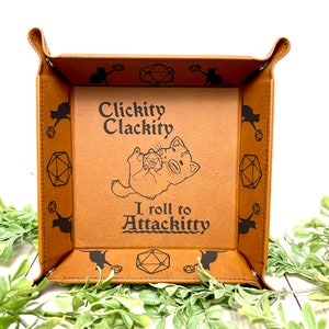 May include: A brown leather dice tray with a cat illustration and the text "Clickity Clackity I roll to Attackitty".
