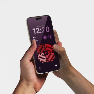 Könnte beinhalten: Ein goldfarbenes Smartphone mit einem lila Bildschirm, der die Uhrzeit, das Wetter und eine rot-rosa Grafik anzeigt. Das Telefon wird mit zwei Händen vor einem hellgrauen Hintergrund gehalten.