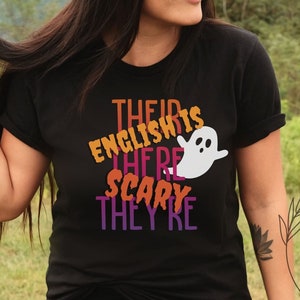 May include: Black t-shirt with a white ghost graphic and the text "Their English is there scary they're" in orange, pink, and purple.