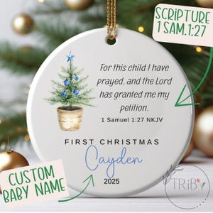 May include: A white ceramic Christmas ornament featuring a watercolour Christmas tree design, blue baubles, and a star. Text includes "First Christmas", "Cayden", "2025", and a Bible verse. A gold string is attached for hanging.