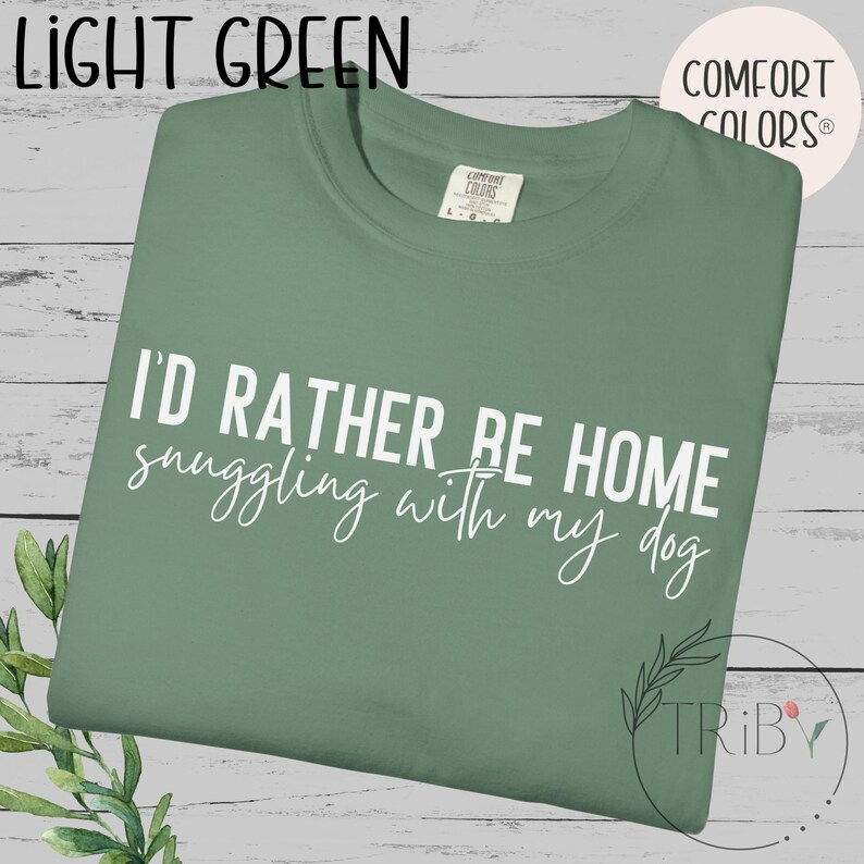 May include: Light green t-shirt with the text "I'd rather be home snuggling with my dog" in white script. The shirt has a crew neck and a tag that says "Comfort Colors".