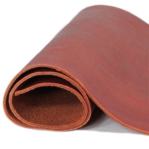 May include: Rolled-up sheet of reddish-brown leather. The leather has a textured surface and appears to be flexible. The edges of the leather are visible, showing the thickness and layers. This leather could be used for crafting.